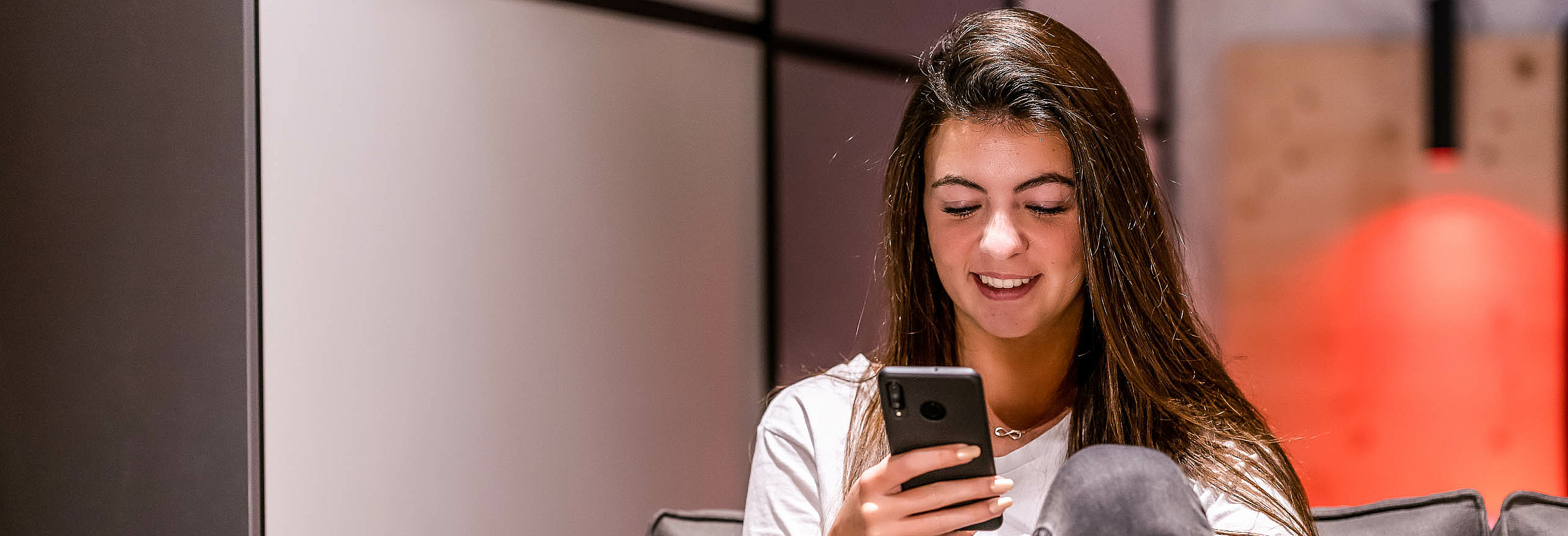 Frau sitzt mit Smartphone in der Hand am Sofa