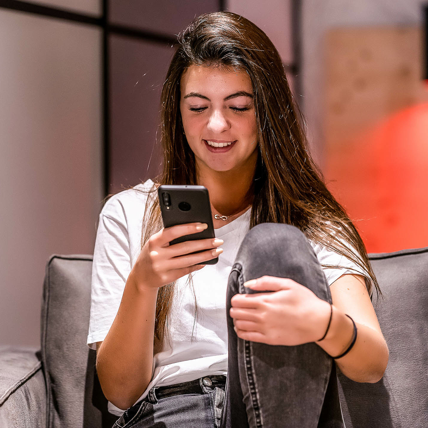 Frau sitzt mit Smartphone in der Hand am Sofa