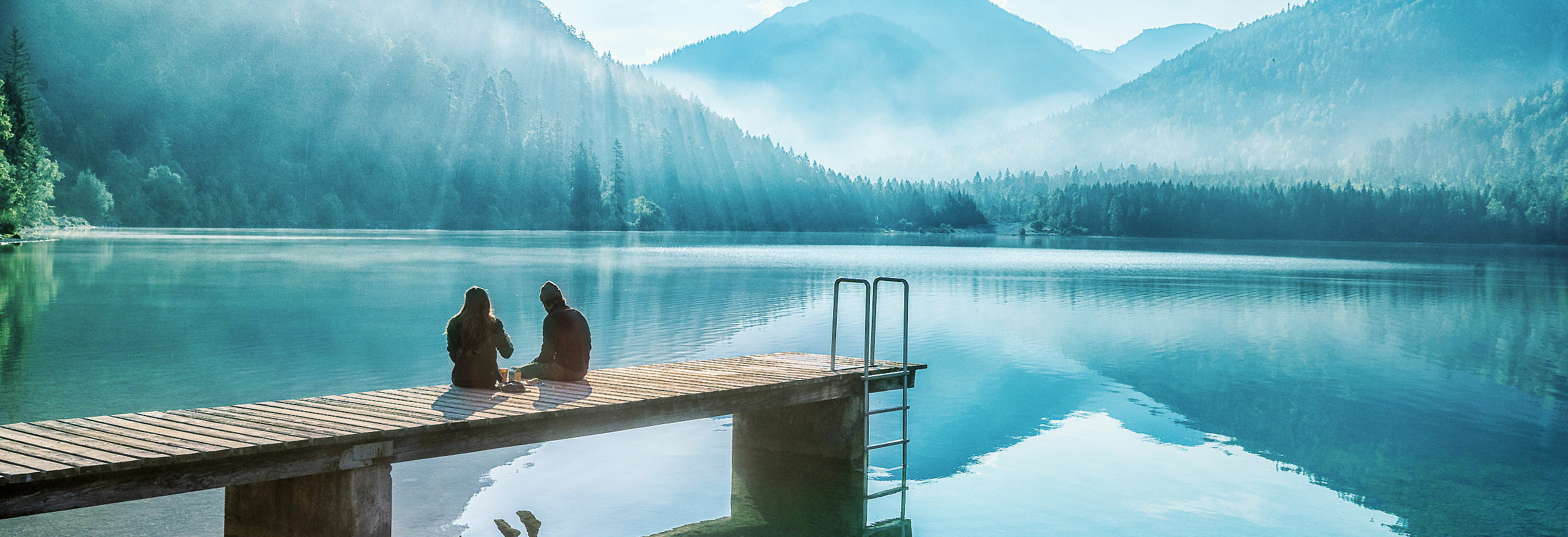 Frau und Mann sitzen auf Steg am See