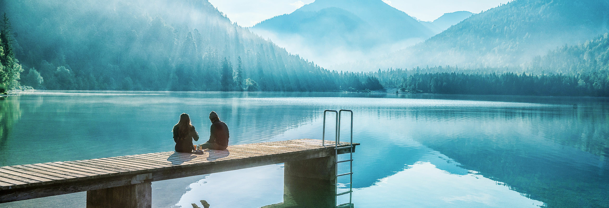 Frau und Mann sitzen auf Steg am See