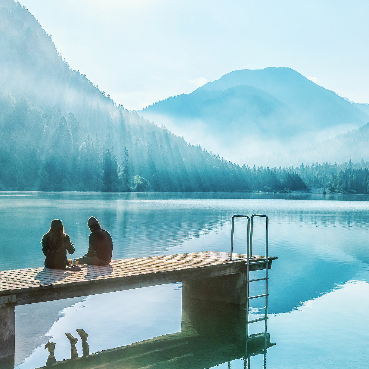 Frau und Mann sitzen auf Steg am See