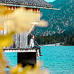 Mann sitzt bei Bootshaus am See