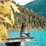 Frau sitzt auf Steg am Seeufer
