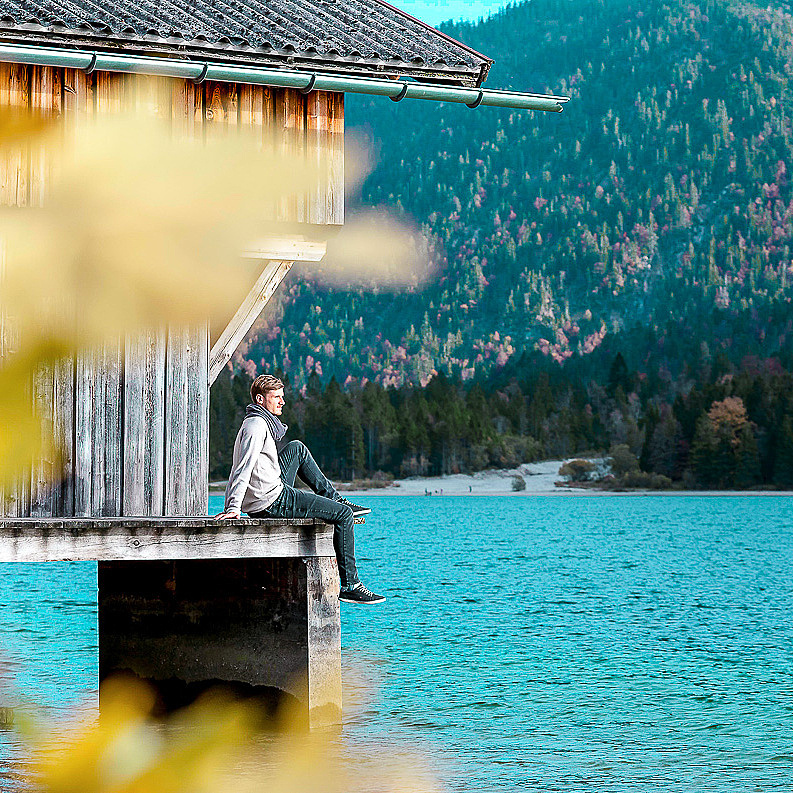 Mann sitzt bei Bootshaus am See