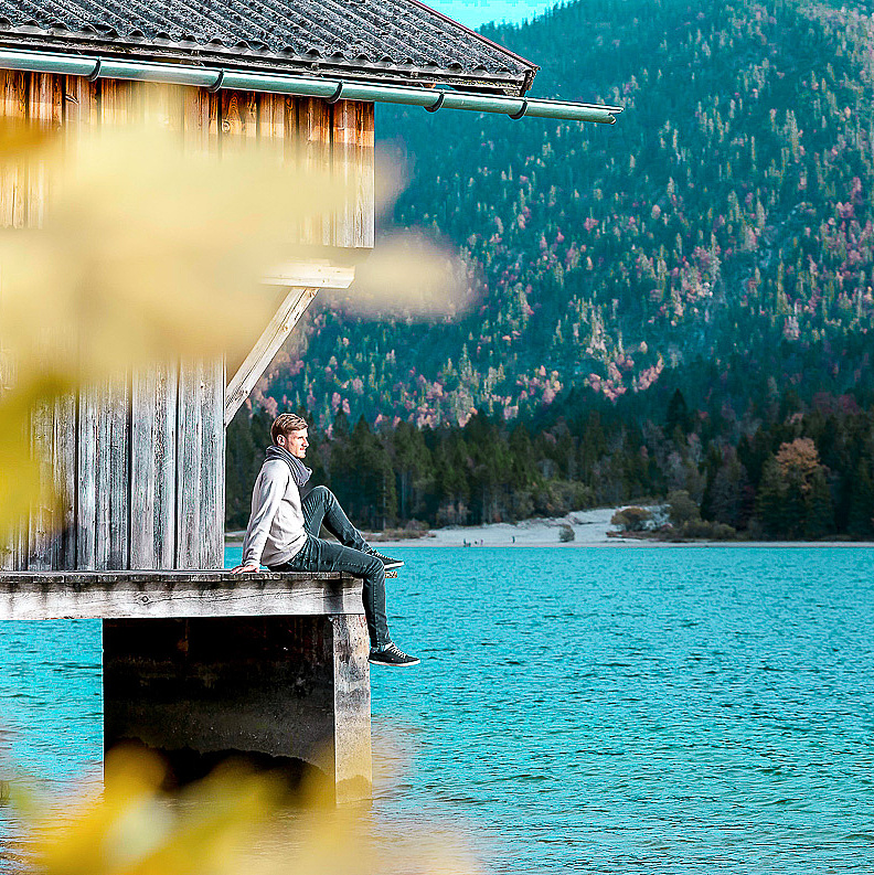 Mann sitzt bei Bootshaus am See