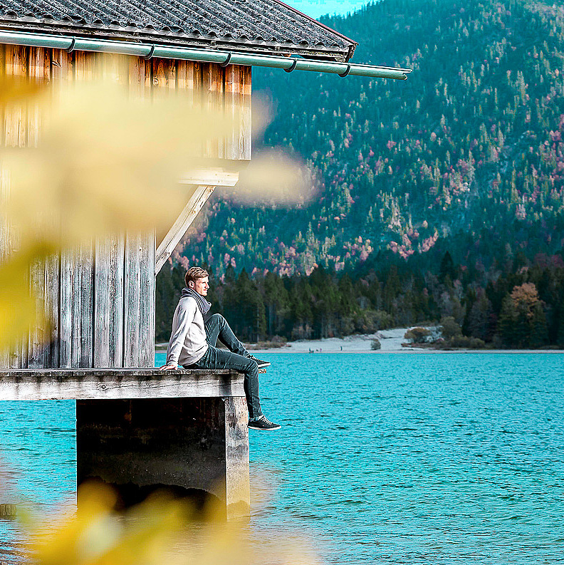 Mann sitzt bei Bootshaus am See