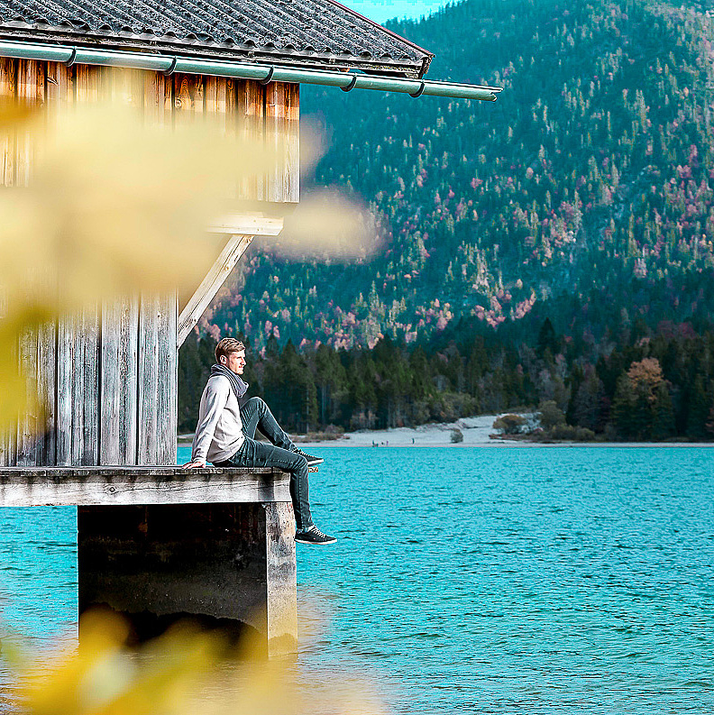 Mann sitzt bei Bootshaus am See