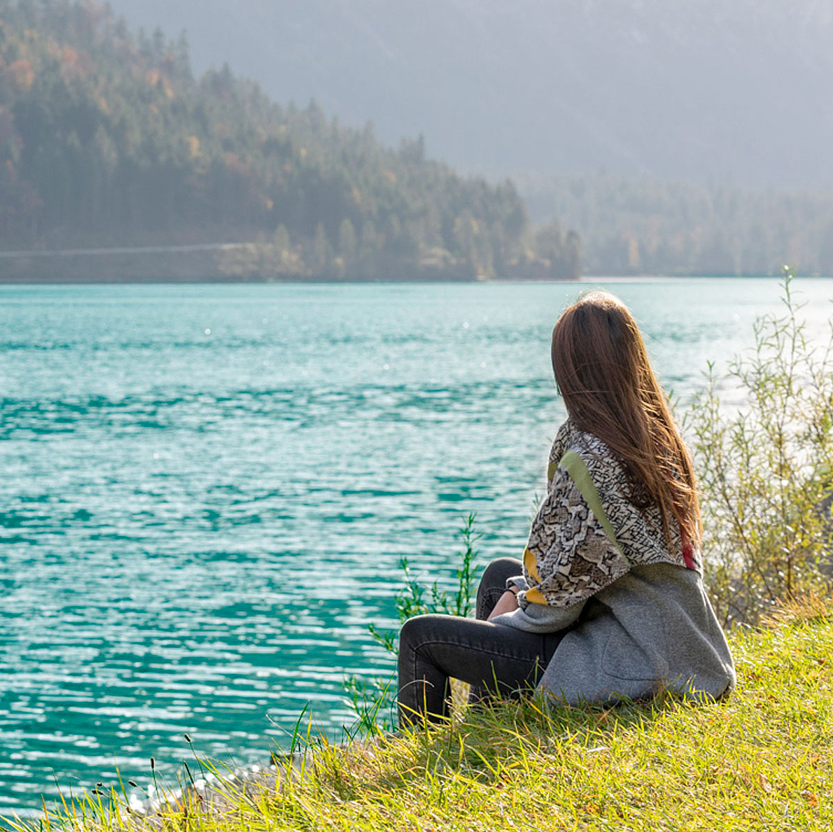 Person sitzt am Ufer eines klaren Sees und blickt auf das Wasser 