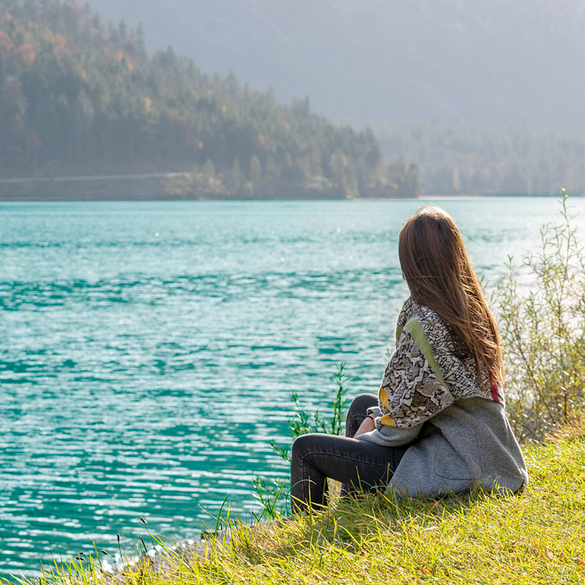 Person sitzt am Ufer eines klaren Sees und blickt auf das Wasser 