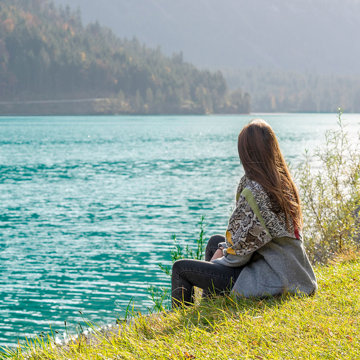 Person sitzt am Ufer eines klaren Sees und blickt auf das Wasser 
