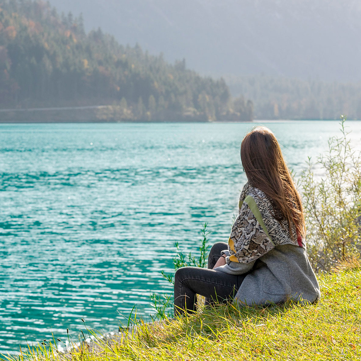 Person sitzt am Ufer eines klaren Sees und blickt auf das Wasser 