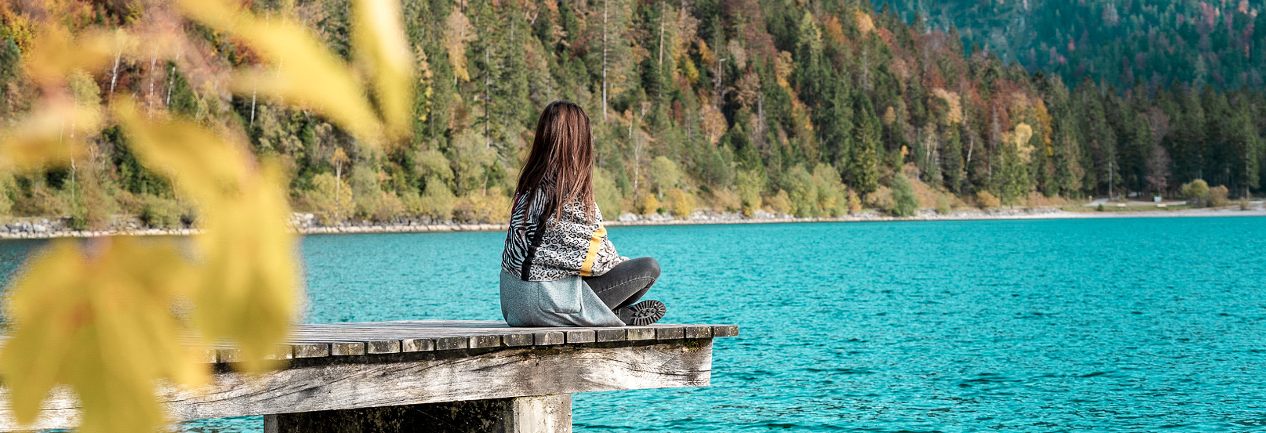 Frau sitzt auf Steg am Seeufer