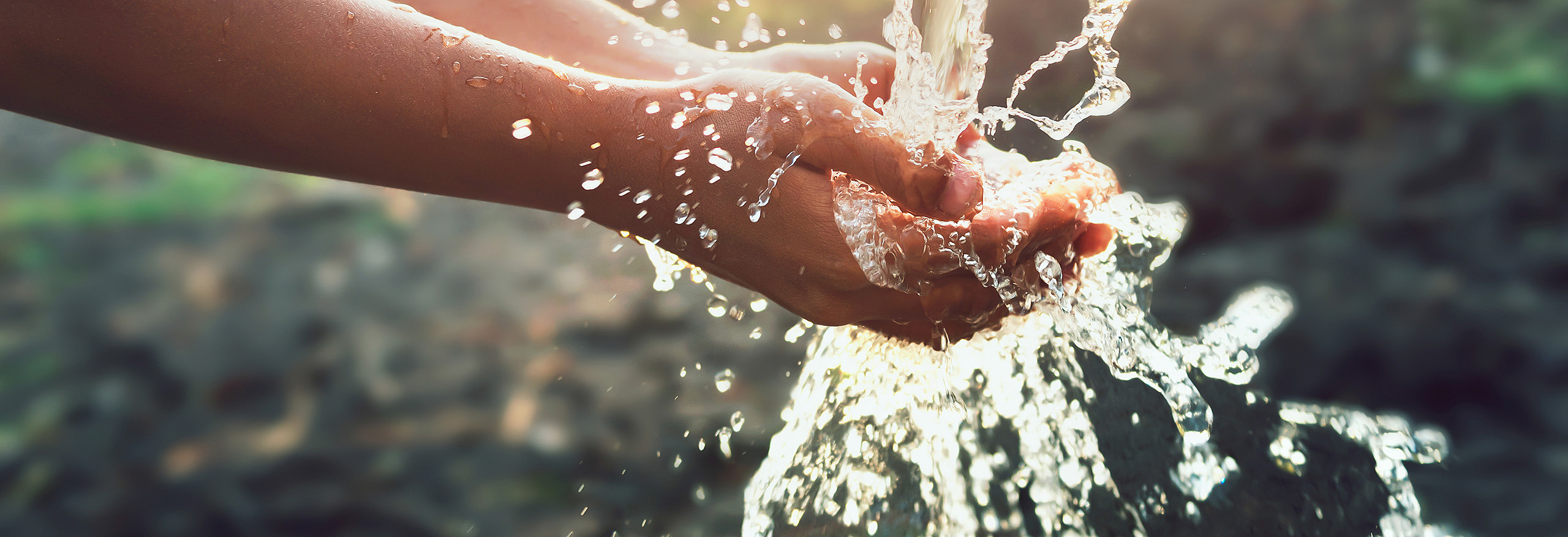 Hände fangen klares Wasser aus einer Quelle oder Leitung im Freien