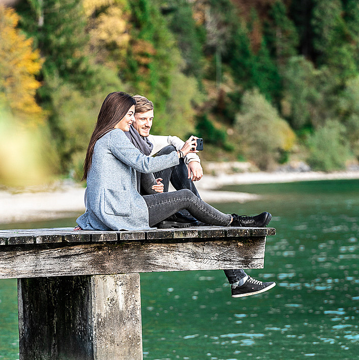 Frau und Mann sitzen auf Steg am Seeufer
