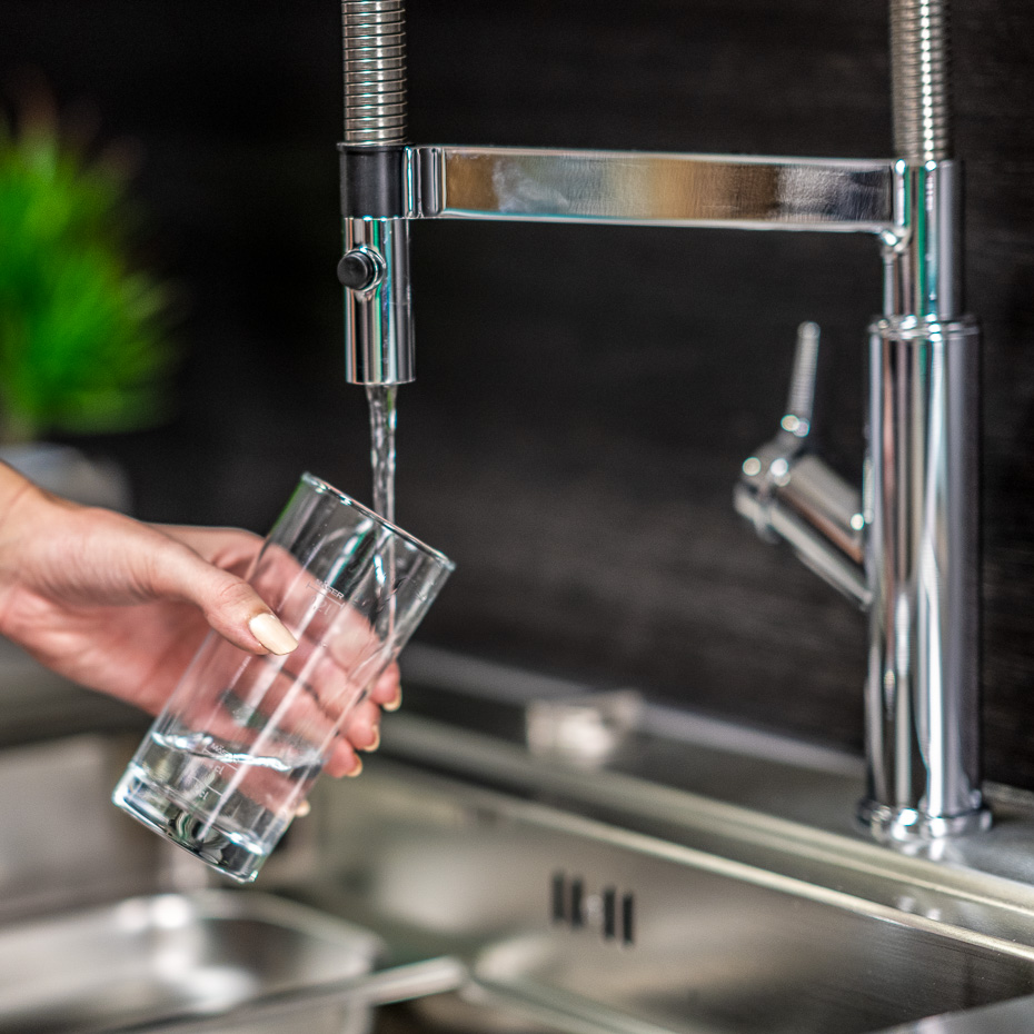 Frau schenkt sich aus Wasserhahn ein Glas Leitungswasser ein