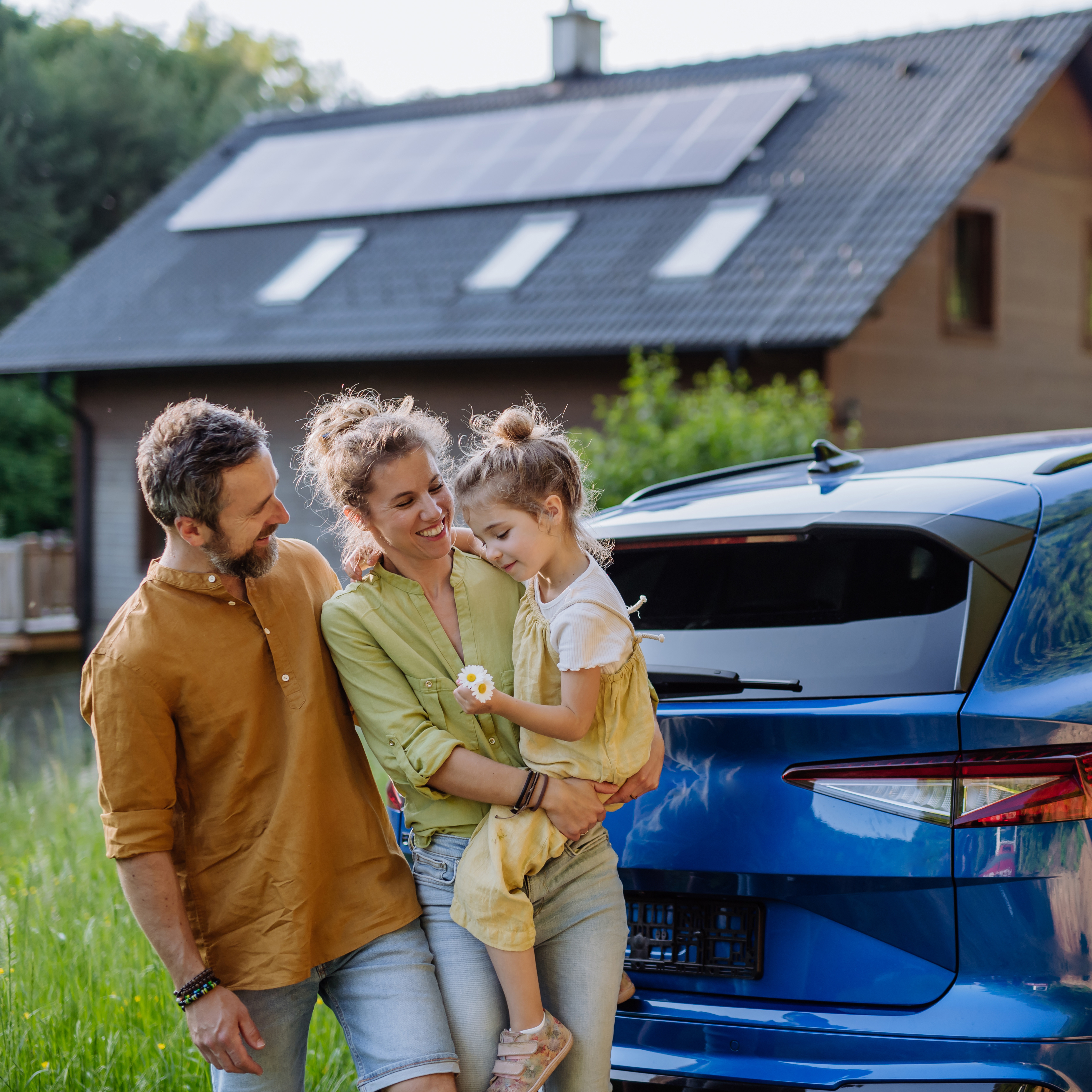 Familie mit Kind steht vor Haus mit Solaranlage und Elektroauto